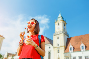 Attractive young woman eating fresh fruit salad while walking through the historic center of the...