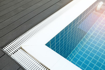 Corner of full water swimming pool on wood floor and white plastic grille at the border