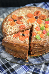 Homemade air-nut cake with chocolate cream, boiled condensed milk, candied fruit, nuts and dried apricot on grey wooden background.