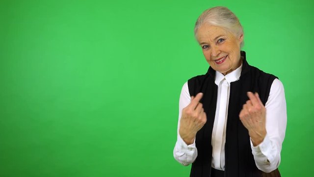 An elderly woman smiles and motions to the camera in a gesture of invitation - green screen studio