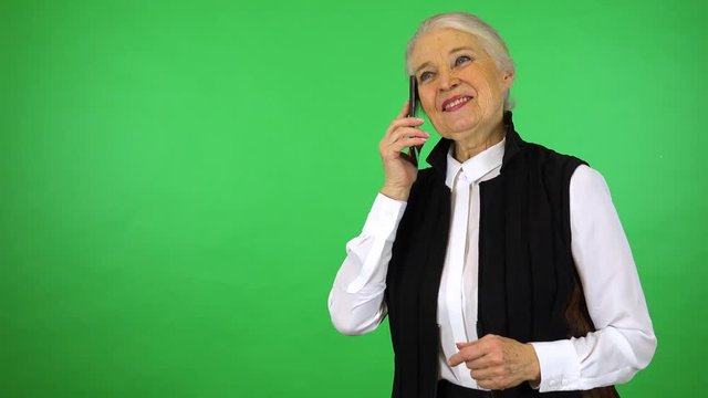 An elderly woman talks on a smartphone with a smile - green screen studio
