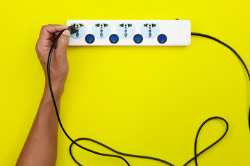 Hand male holding electric plug and putting plug Into multiple socket with connected plugs on yellow paper background.