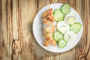 oiled chicken breast with fried eggs and cucumber on white plate on wooden background. Healthy lunch or dinner.