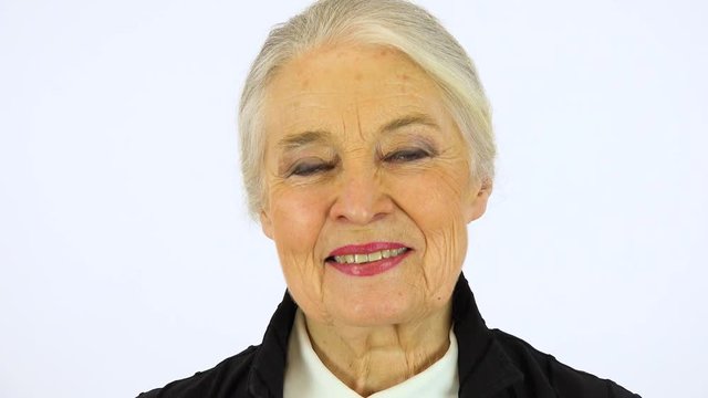 An elderly woman smiles at the camera - face closeup - white screen studio