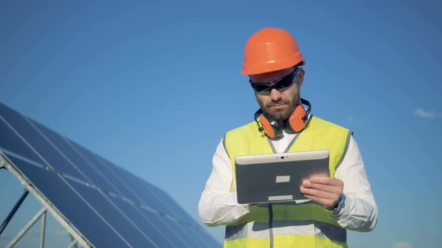 Working process of a male inspector standing with a computer nearby the solar panel