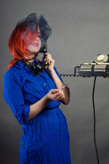 A girl with red hair in a blue dress with a cigarette rings an old phone