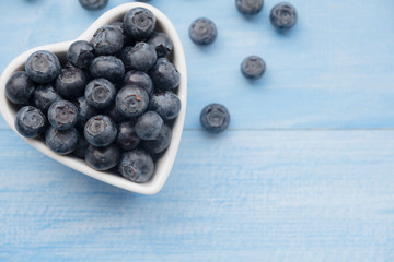 Fresh ripe blueberries fruits in love heart ceramic cup bowl on wooden table. Concept about love and relationship. Healthy fruits clean diet foods, with copy space, top view.