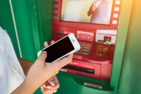 Woman Holding Mobile Phone With Black Screen And A Credit Card At An ATM. Security Code On An Automated Teller Machine