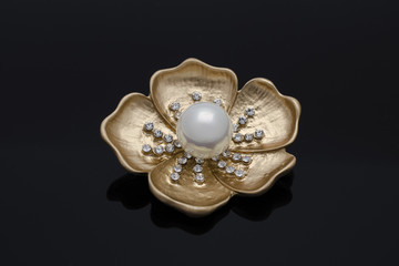 gold brooch flower with a pearl and diamonds isolated on black