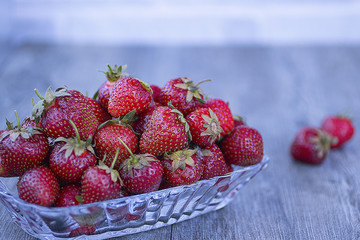 Ripe strawberries in a glass plate on a gray background.