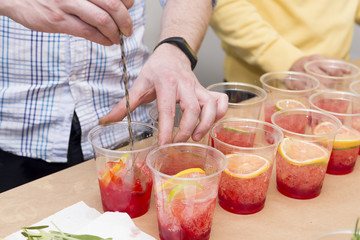 man prepares a cocktail, a lot of cups with a drink of red color and with slices of lemon and lime