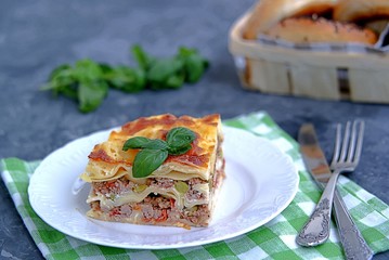 Lasagna with pork forcemeat, green peas and tomatoes on a dark gray concrete background.