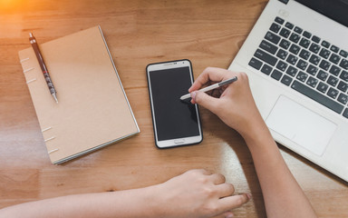 Top View of woman hands using blank white laptop on wooden surface with notepad.