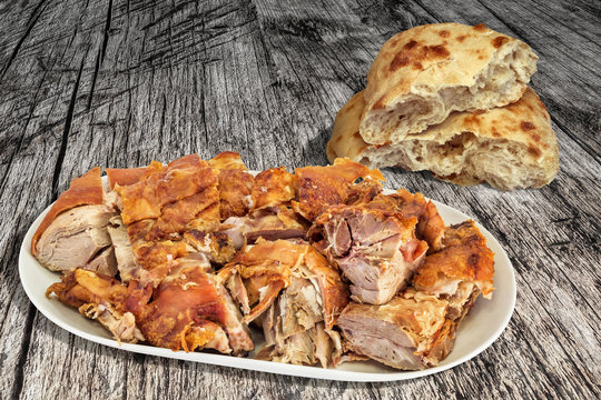Plateful of fresh roasted pork shoulder slices and leavened flatbread torn loaf set on old weathered cracked pinewood garden table