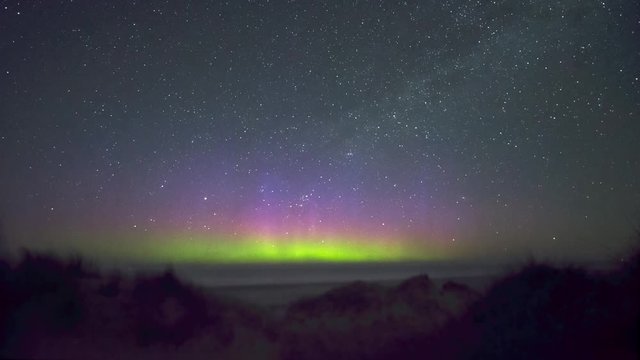 distant northern lights over the ocean seen from the beach