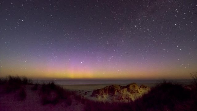 distant northern lights over the ocean seen from a moonlit dune landscape
