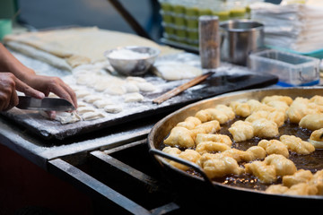 Thai fried bread sticks Potongko, frying in a pot while helper in the background is preparing the dough