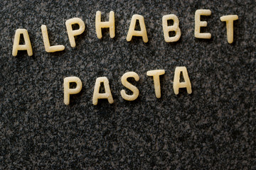 Raw Alphabet Pasta is Written with Letters  on Granit Grey Surface.