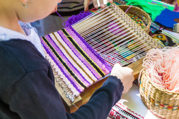 Hands of a girl weaving a Ukrainian mat made of multi-colored threads.