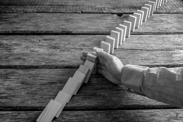 Monochrome image of a businessman preventing dominoes from crumbling
