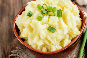 Mashed potatoes in bowl on wooden table with spring green onion and garlic.