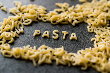 Raw Alphabet Pasta is Written with Letters  on Granit Grey Surface.