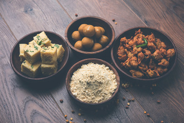 Chick pea flour or Besan powder in a ceramic or wooden bowl along with Gujrati Dhokla snack, onion bajji or bhaji and sweet laddu or laddoo