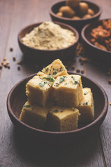 Chick pea flour or Besan powder in a ceramic or wooden bowl along with Gujrati Dhokla snack, onion bajji or bhaji and sweet laddu or laddoo