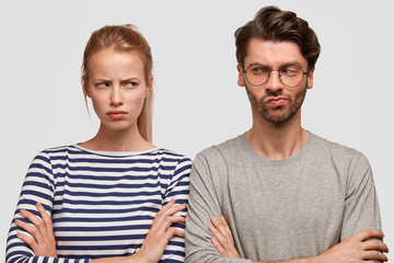 Gloomy female with unhappy expression, keeps hands crossed, looks angrily at boyfriend, have quarrel. Family couple sort out relationship, argue and complain about something. Relationship problem