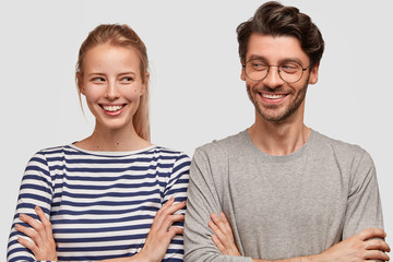 Two best friends look joyfully at each other, keep arms folded, have grandiose plan in mind, broad...