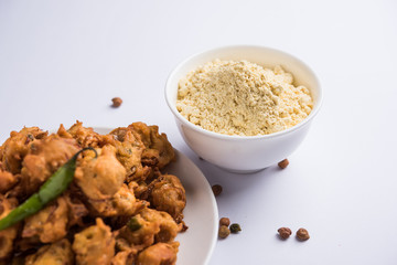 Chick pea flour or Besan powder in a ceramic or wooden bowl along with fried onion pakora or kanda bajji
