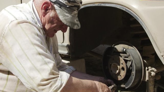 Senior man engaged in the repair of an old car in the backyard