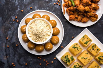 Chick pea flour or Besan powder in a ceramic or wooden bowl along with Gujrati Dhokla snack, onion bajji or bhaji and sweet laddu or laddoo