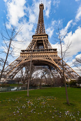 Wide angle view of iconic Eiffel tower with dramatic cloudy blue sky in the background.