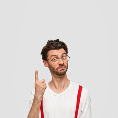Intelligent male student has brilliant solution in mind, raises fore finger, looks with proud and...