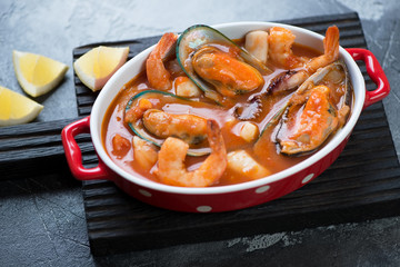 Bowl of buyabes or french fish soup on a black wooden serving board, studio shot