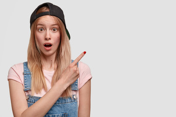 Studio shot of stunned beautiful teenager dressed in casual clothes, wears black cap on head, feels...