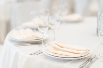 Festive table setting at a banquet in white. White plates, napkins and tablecloth in a restaurant