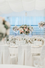 Festive decoration of the wedding celebration in the banquet hall with white tablecloths and flowers