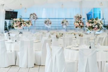 Festive decoration of the wedding celebration in the banquet hall with white tablecloths and flowers