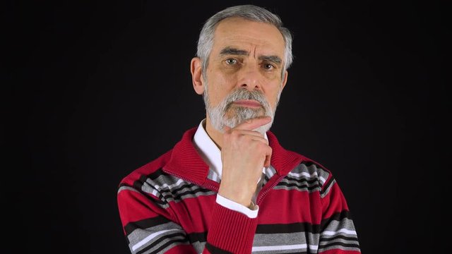 An elderly man looks at the camera with interest - black screen studio
