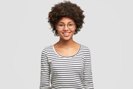 Positive emotions concept. Happy young smiling African American female in spectacles, rejoices unforgettable party with friend, dressed in casual striped jacket, isolated on white background