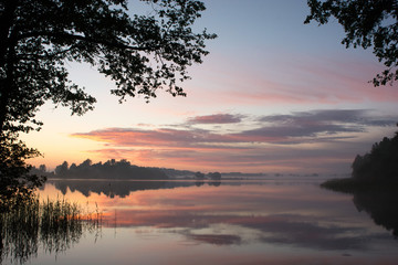 Fototapeta premium The sun setting over a lake during summertime 