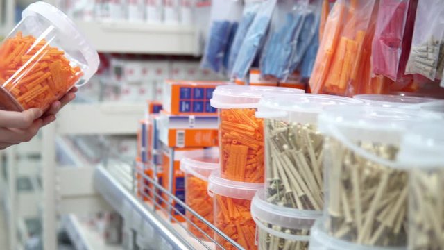 A young woman chooses a transparent container with orange corrugated plastic plugs in the store. She is preparing for repair or construction.