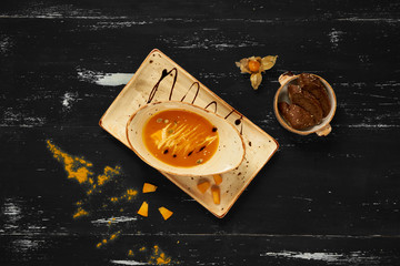 Tasty creamy pumpkin soup in oval bowl and rectangular plate standing on blue aged wooden table. Appetizing restaurant vegan meal served with bread slices, delicious veggie recipe. Top view.