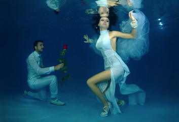 Groom kneeling gives flowers to the bride underwater in the pool. Underwater wedding