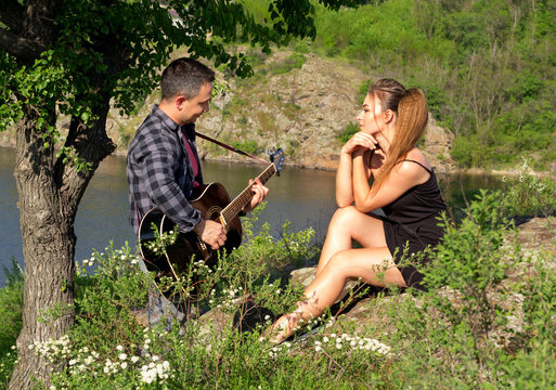 Young attractive man playing guitar for his beautiful girlfriend. Love concept.