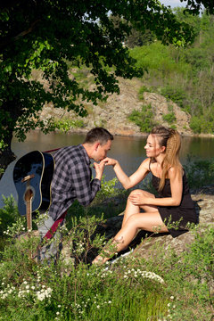 Young attractive man with guitar kissing hand of his beautiful girlfriend in park