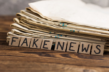 Heap of old newspapers beside cardboard rectangle squares with handwritten inscription fake news on...