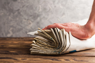 Heap of stacked old newspapers and human hand on old brown wooden table on background of concrete...